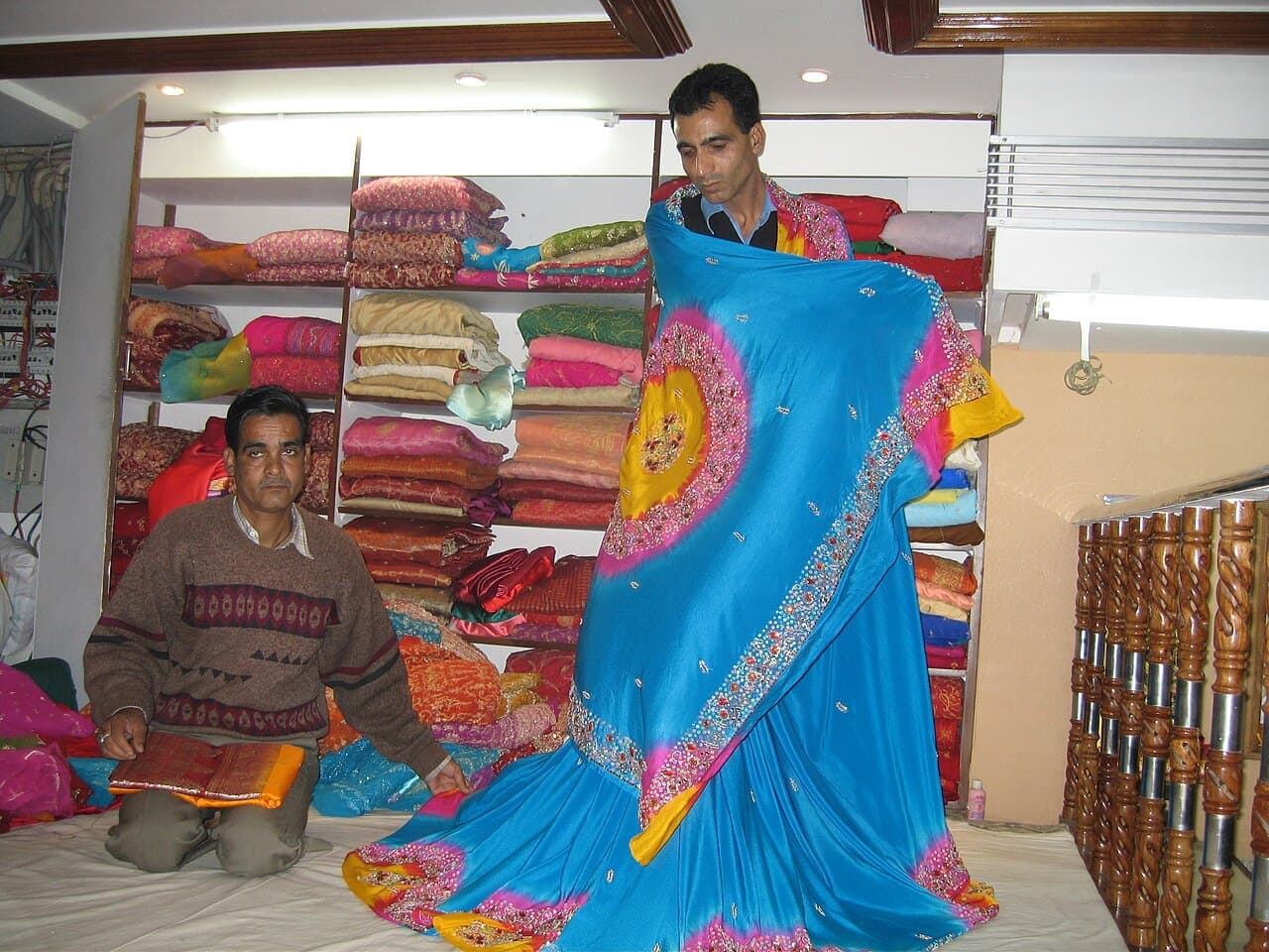 A clothing shop owner and staff member showing a lehenga