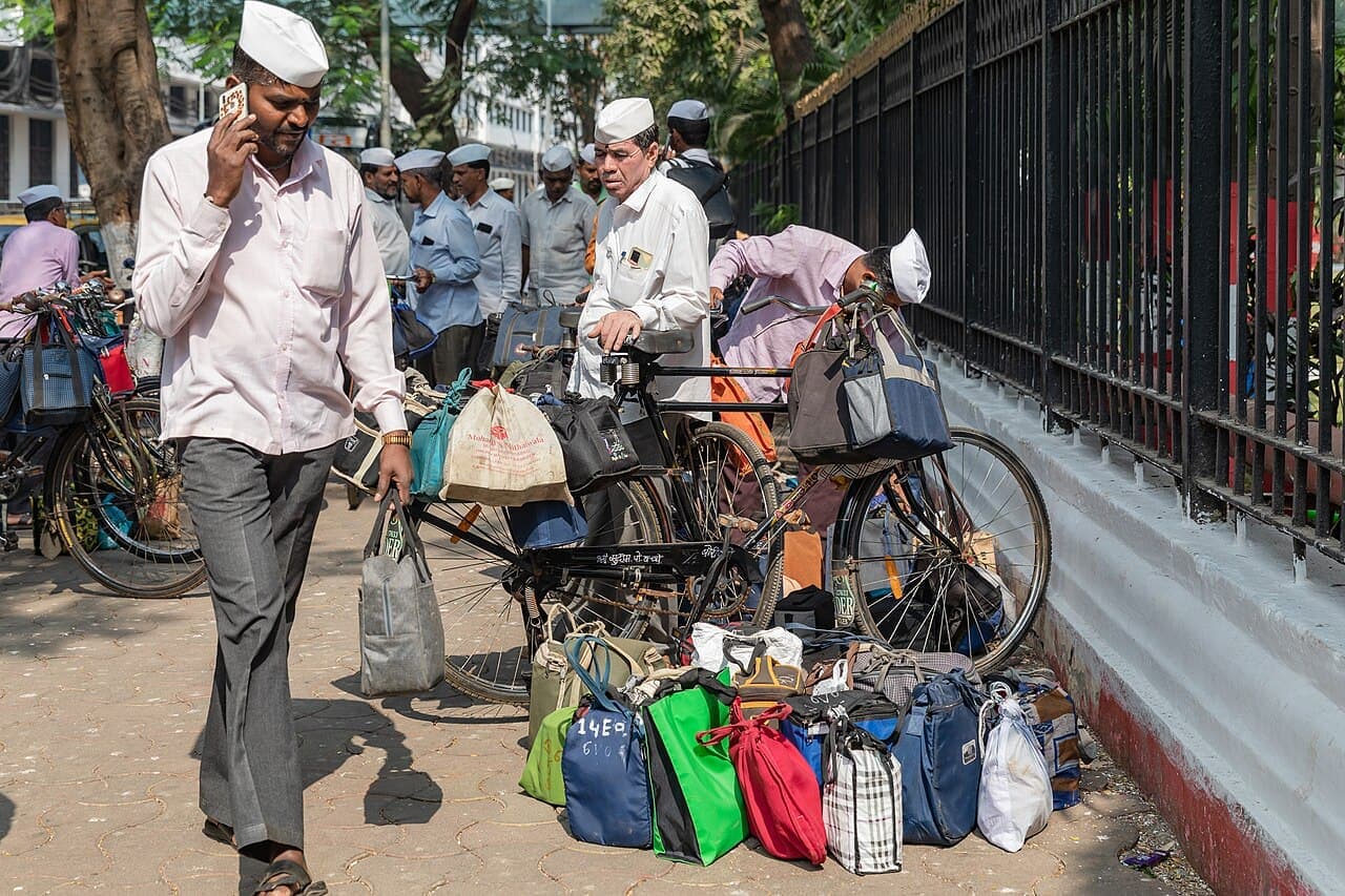 A Mumbai dabbawala on a phone call beside tiffin bags